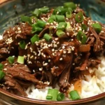 Tender Slow-Cooker Korean Beef served over steamed rice with sesame seeds and green onions.