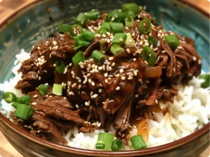 Tender Slow-Cooker Korean Beef served over steamed rice with sesame seeds and green onions.
